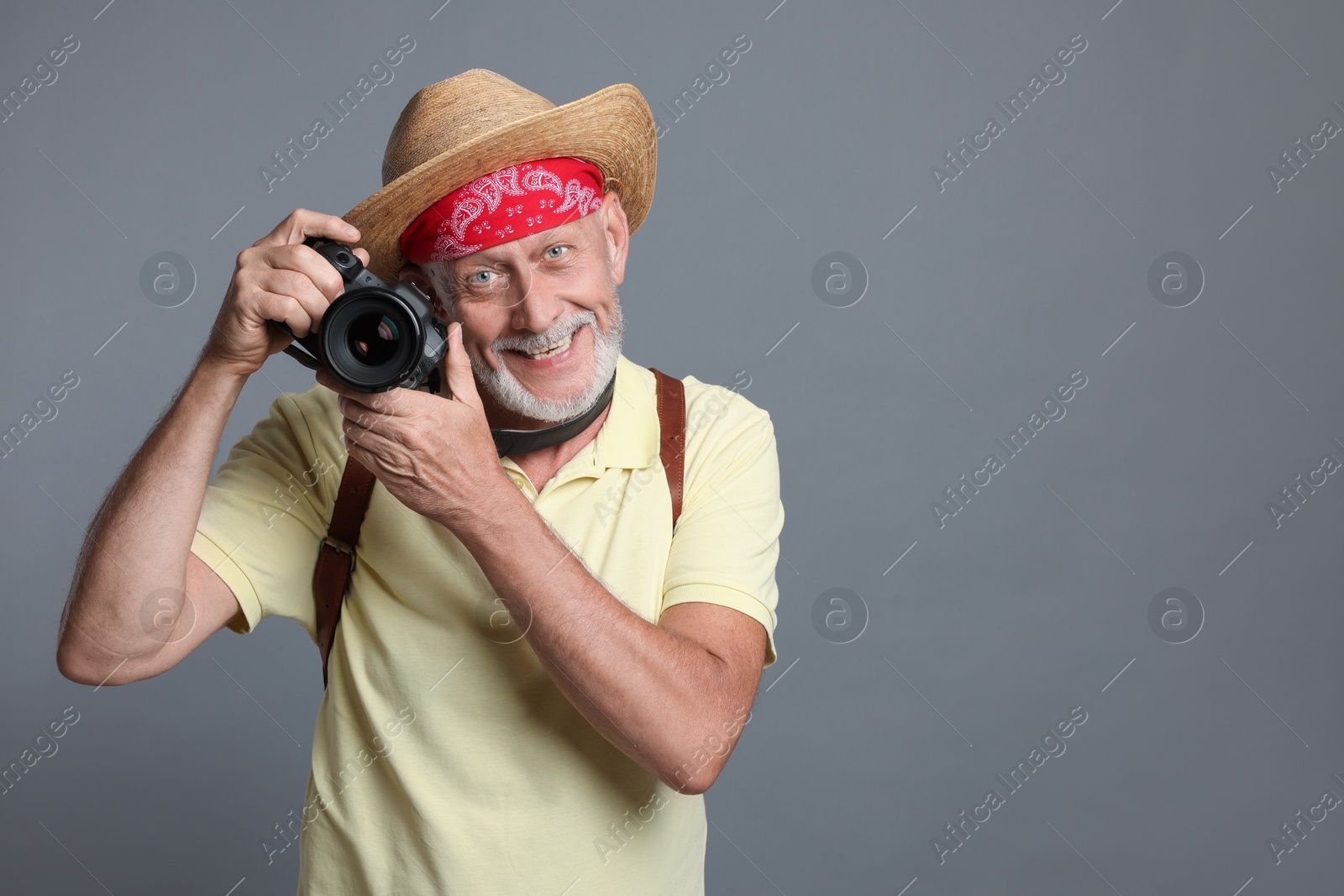 Photo of Portrait of happy senior man with camera on grey background. Space for text