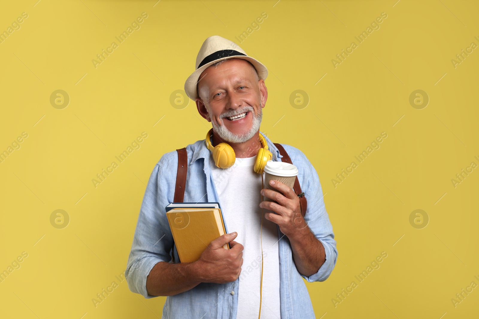 Photo of Portrait of happy senior man with books and paper cup on yellow background