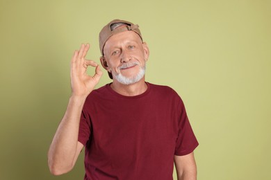 Portrait of handsome senior man showing ok gesture on green background