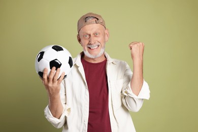 Portrait of emotional senior man with soccer ball on green background