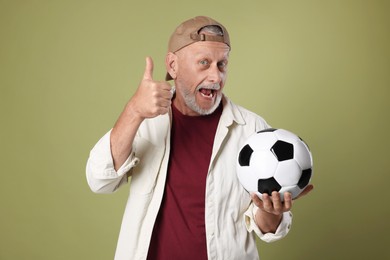 Photo of Portrait of emotional senior man with soccer ball showing thumbs up on green background