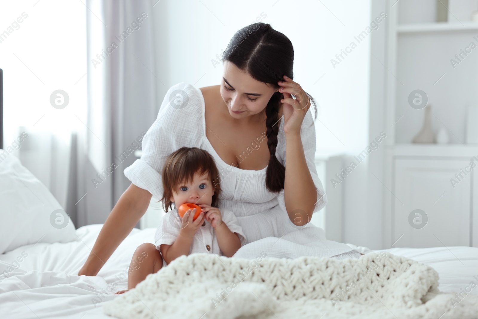 Photo of Beautiful young mother and her cute little baby with toy on bed at home