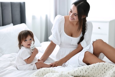 Photo of Beautiful young mother and her cute little baby with rattle on bed at home