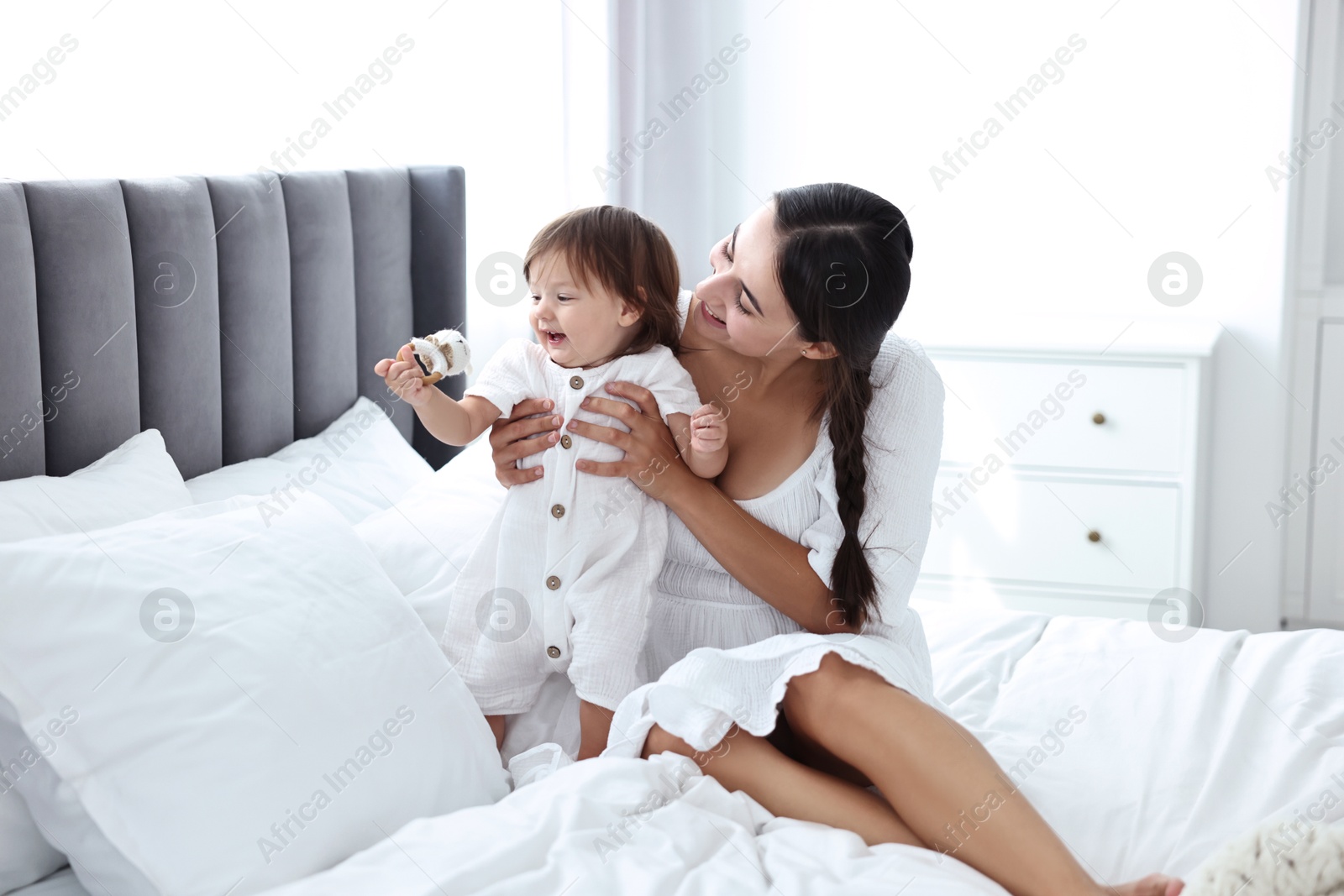 Photo of Beautiful young mother and her cute little baby with rattle on bed at home