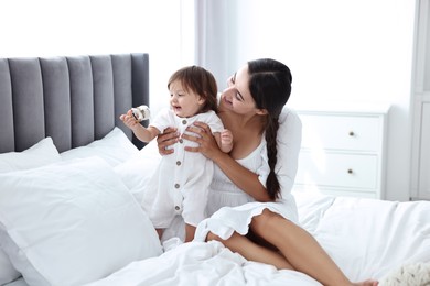 Photo of Beautiful young mother and her cute little baby with rattle on bed at home