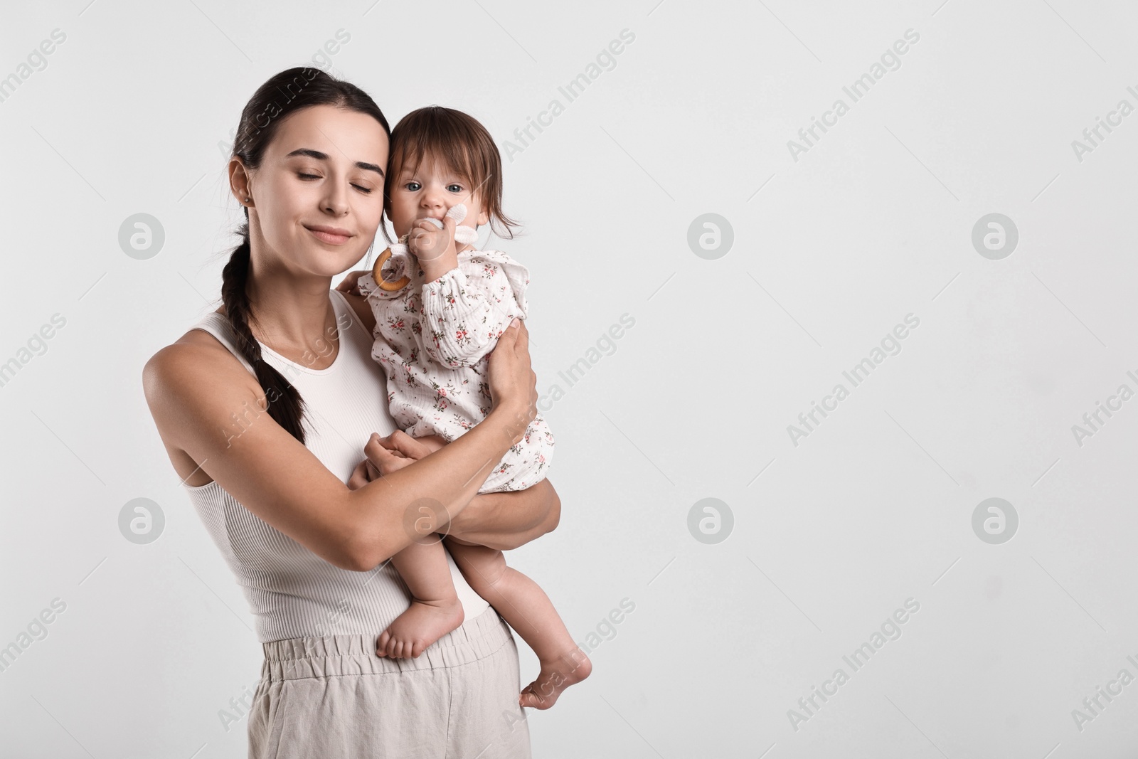 Photo of Beautiful young mother and her cute little baby with rattle on light grey background, space for text