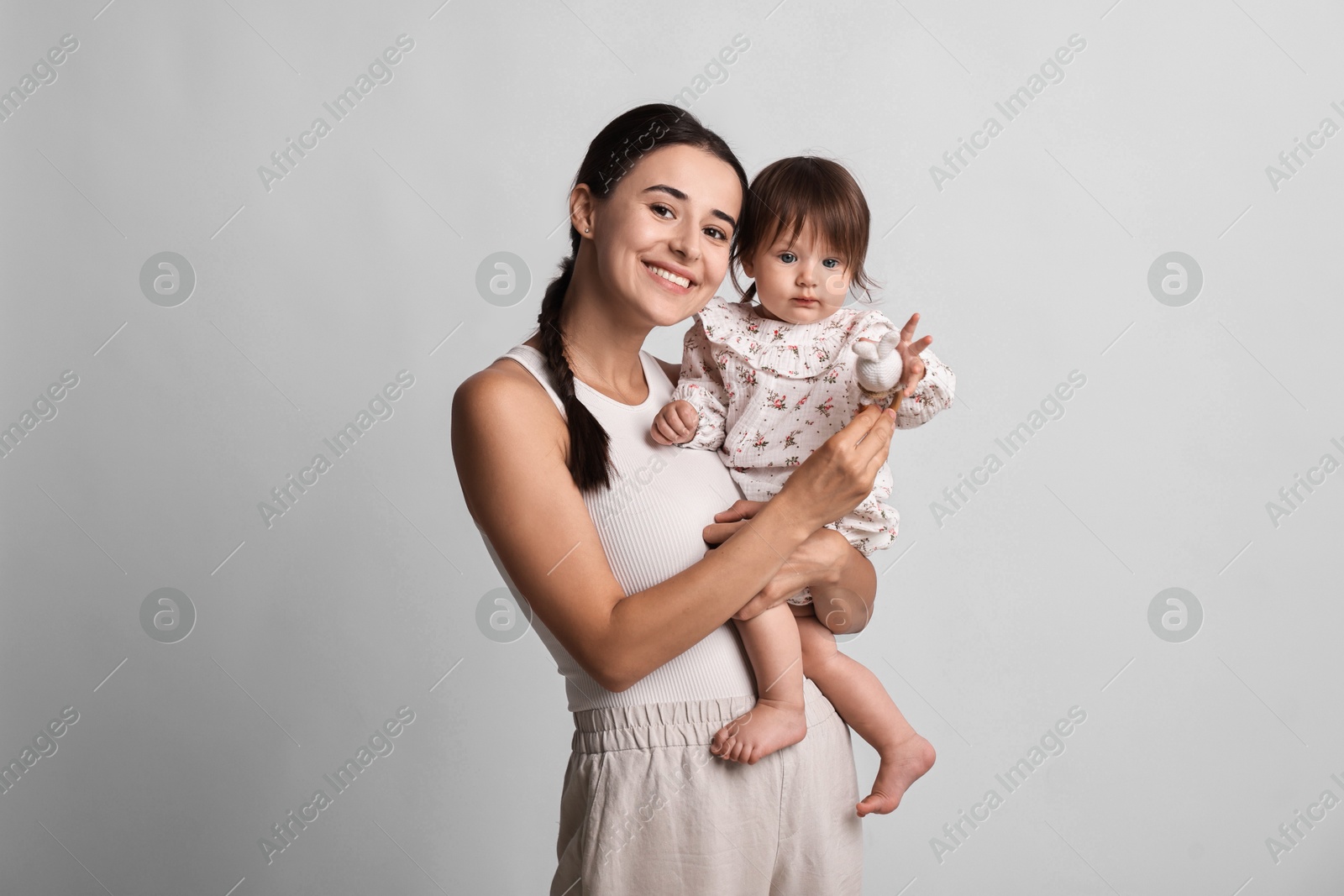 Photo of Beautiful young mother and her cute little baby with rattle on light grey background