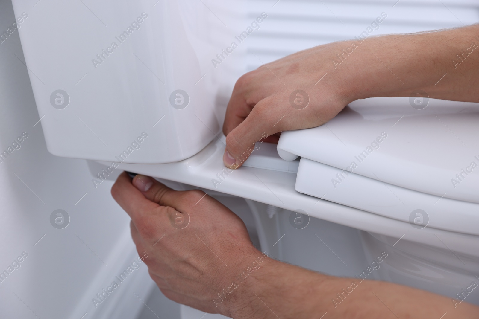 Photo of Man fixing toilet seat in bathroom, closeup