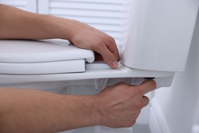 Photo of Man fixing toilet seat in bathroom, closeup