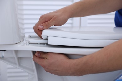 Man fixing toilet seat in bathroom, closeup