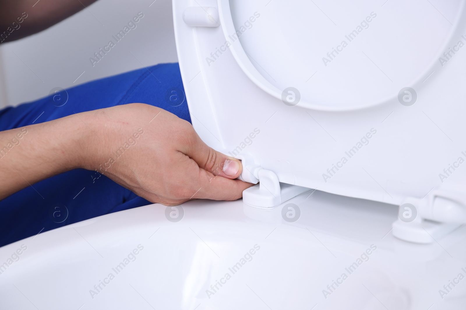 Photo of Man fixing toilet seat in bathroom, closeup