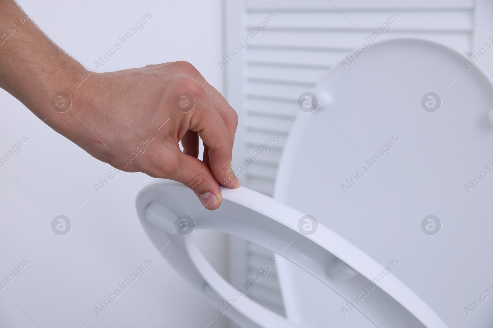 Photo of Man closing toilet seat in bathroom, closeup