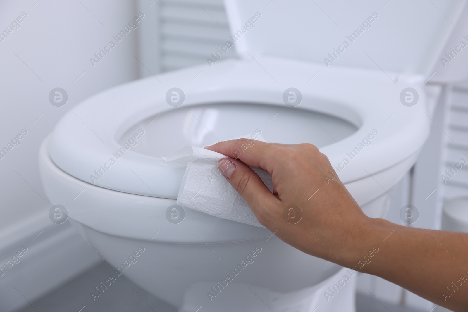 Photo of Woman wiping toilet seat with paper in bathroom, closeup