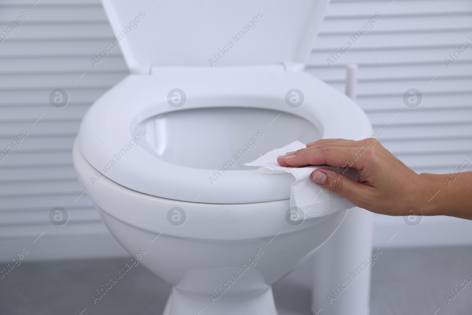 Photo of Woman wiping toilet seat with paper in bathroom, closeup