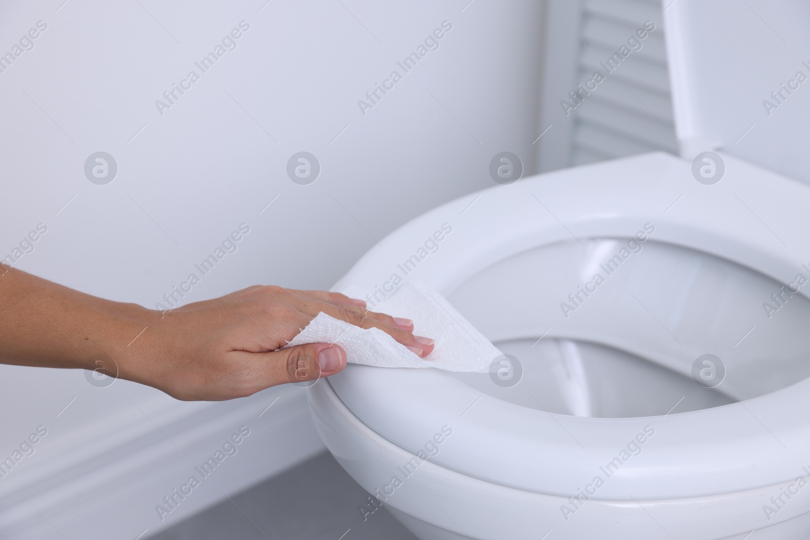 Photo of Woman wiping toilet seat with paper in bathroom, closeup