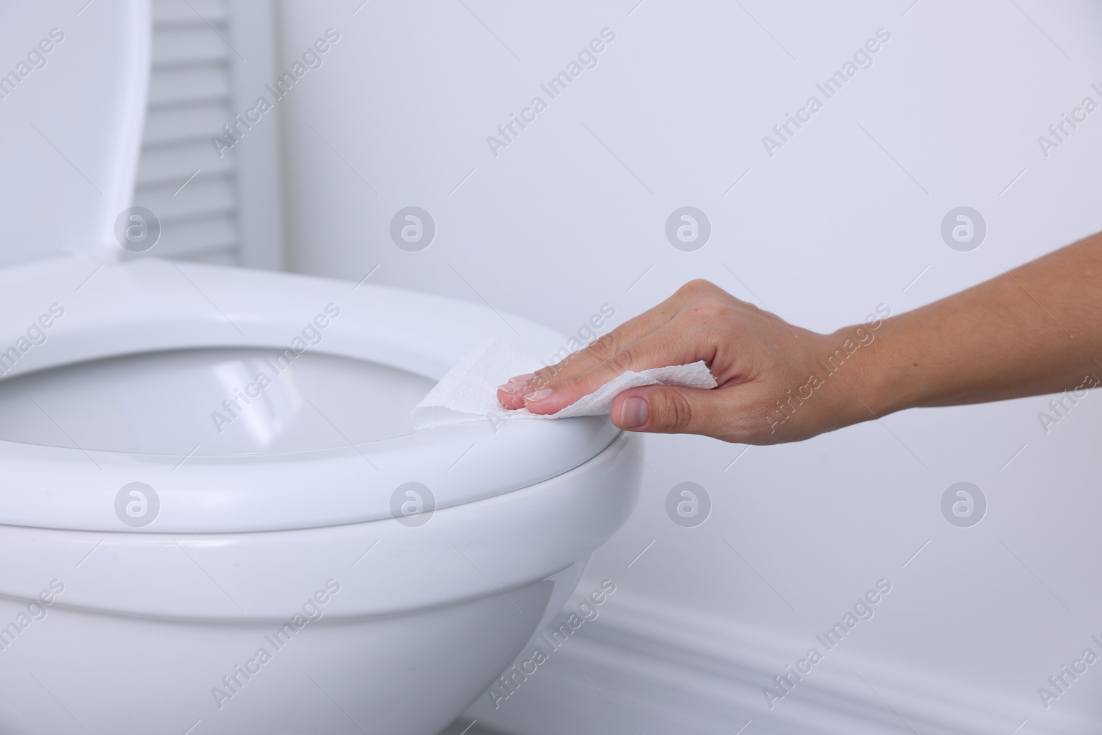 Photo of Woman wiping toilet seat with paper in bathroom, closeup