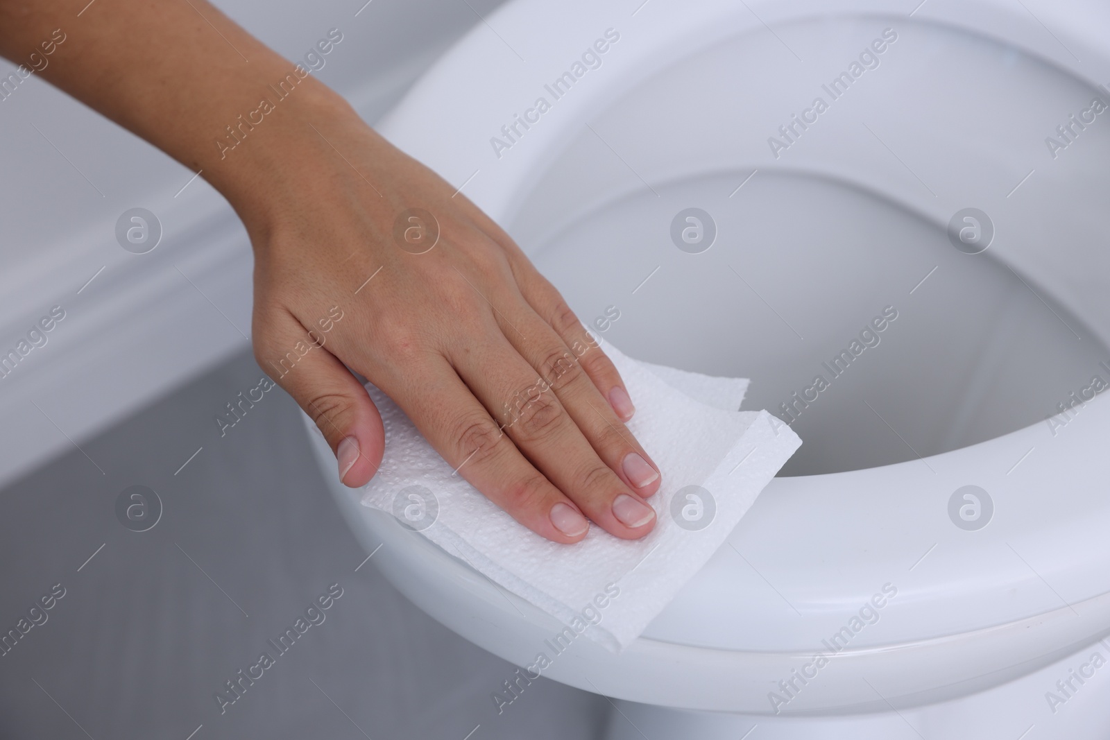 Photo of Woman wiping toilet seat with paper in bathroom, closeup