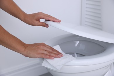 Photo of Woman wiping toilet seat with paper in bathroom, closeup