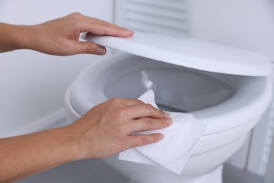 Photo of Woman wiping toilet seat with paper in bathroom, closeup