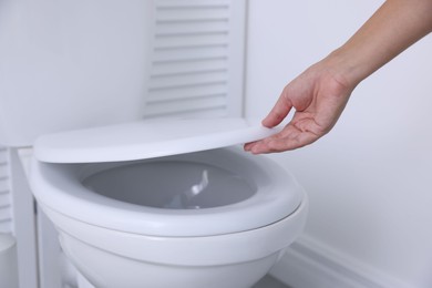 Photo of Woman closing toilet seat in bathroom, closeup