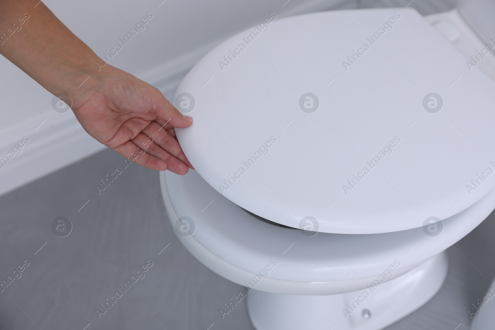 Photo of Woman closing toilet seat in bathroom, closeup