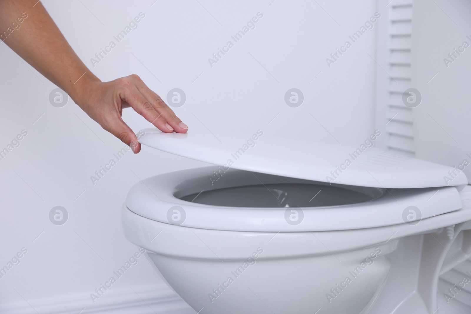 Photo of Woman closing toilet seat in bathroom, closeup