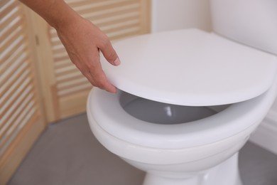 Photo of Woman closing toilet seat in bathroom, closeup