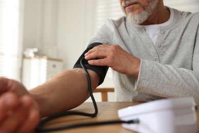 Photo of Senior man measuring blood pressure at table indoors, closeup