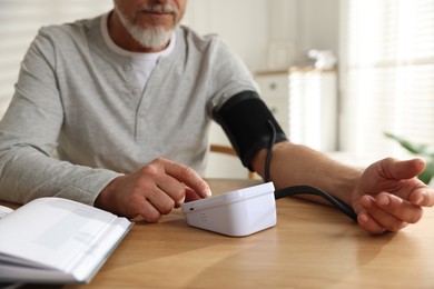 Photo of Senior man measuring blood pressure at wooden table indoors, closeup