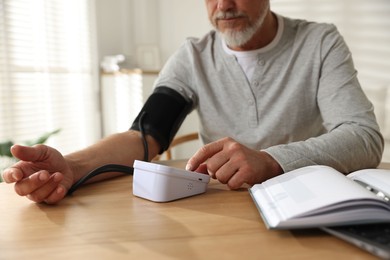 Photo of Senior man measuring blood pressure at wooden table indoors, closeup