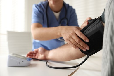 Photo of Doctor measuring patient's blood pressure at table indoors, closeup