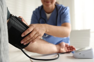 Photo of Doctor measuring patient's blood pressure at table indoors, closeup