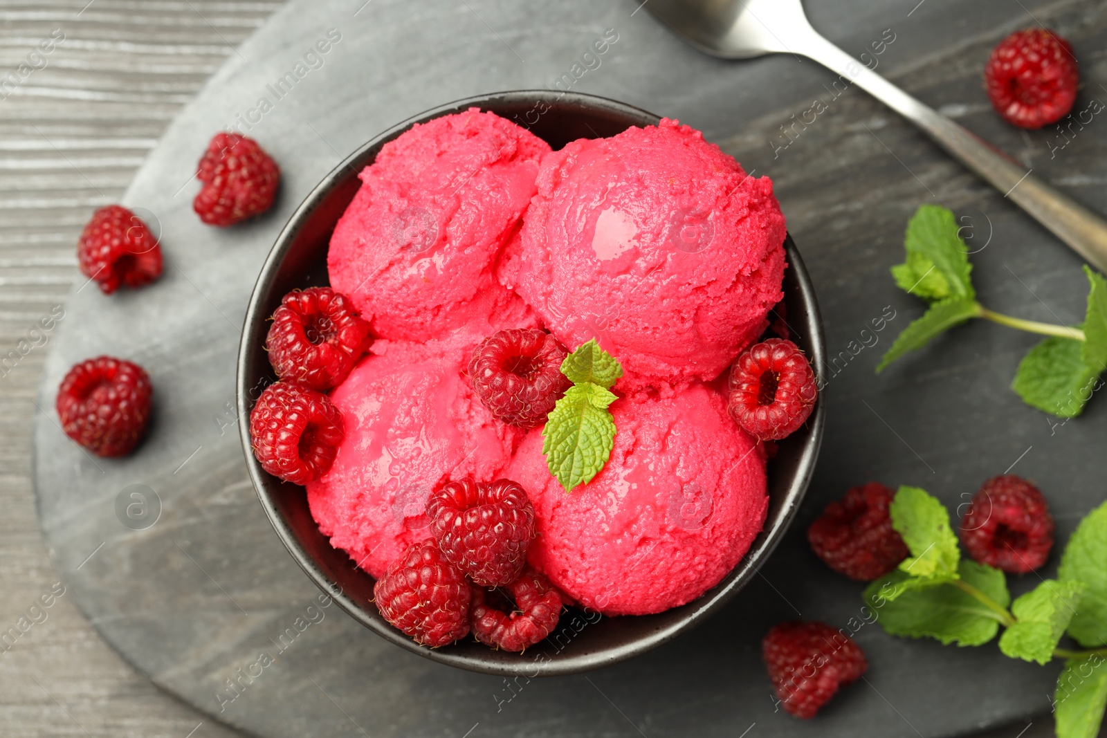 Photo of Delicious raspberry sorbet in bowl, fresh berries, mint and spoon on wooden table, top view