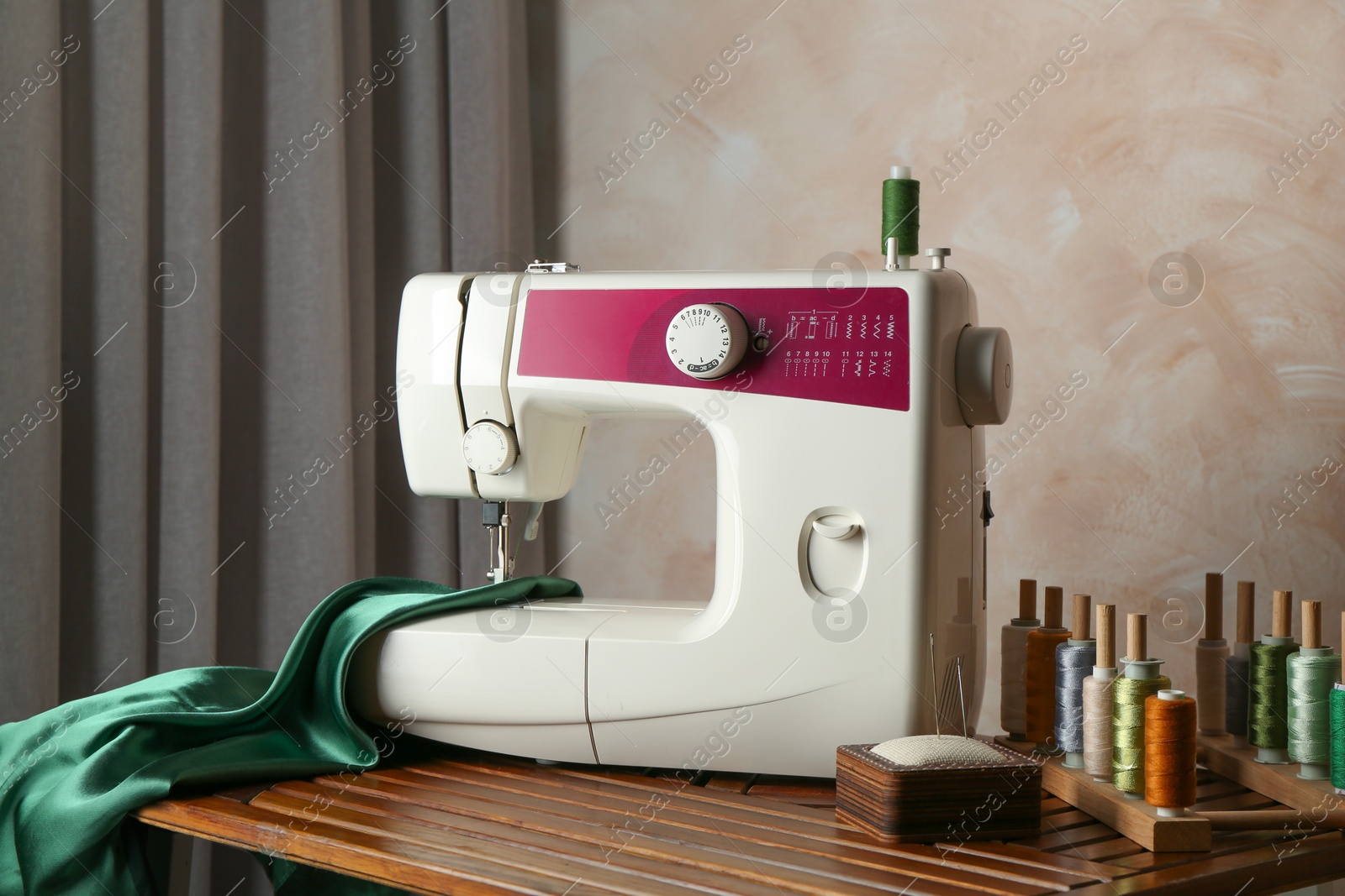 Photo of Sewing machine, green fabric and craft accessories on wooden table indoors