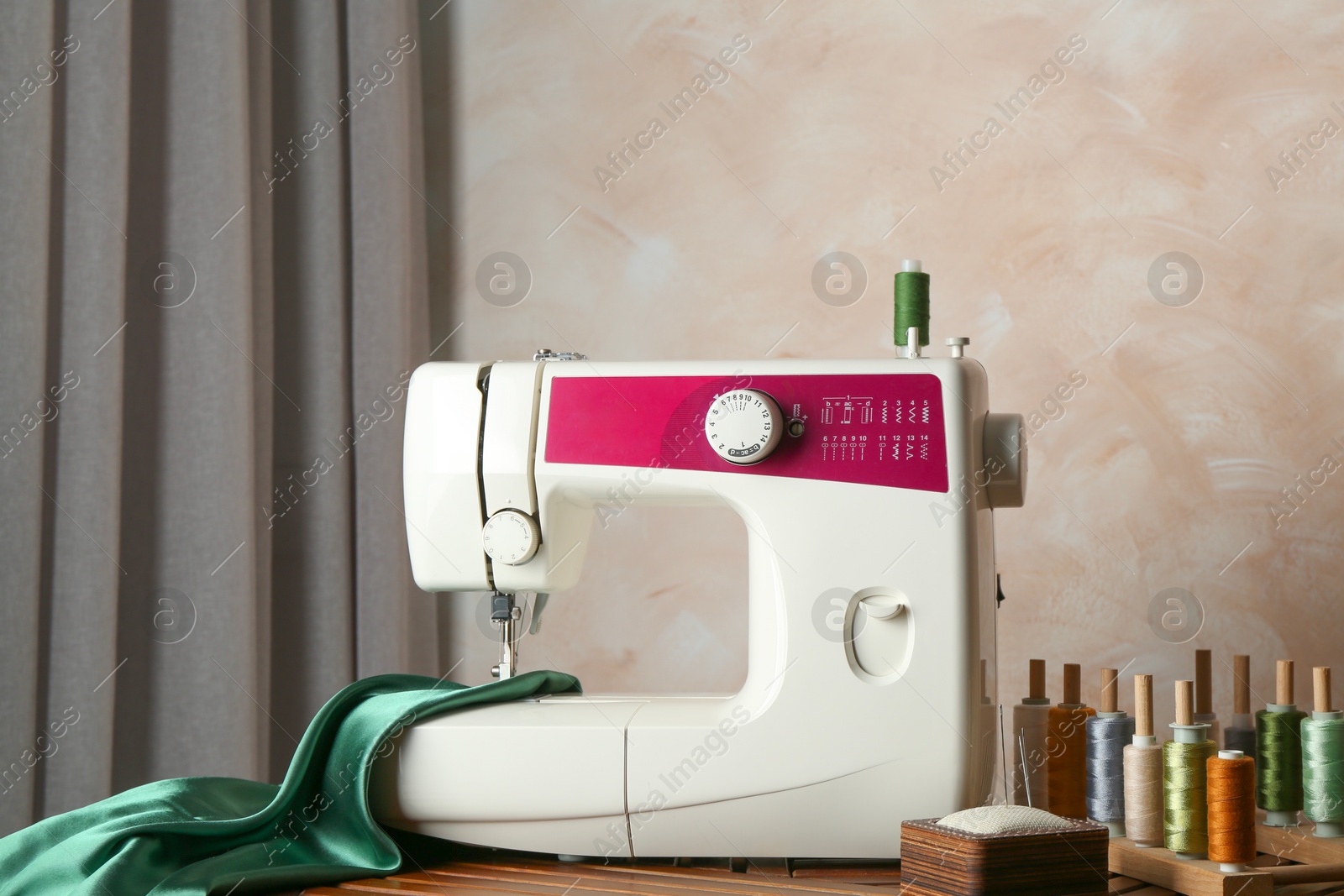 Photo of Sewing machine, green fabric and craft accessories on wooden table indoors