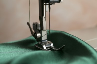 Photo of Sewing machine with green fabric on light background, closeup