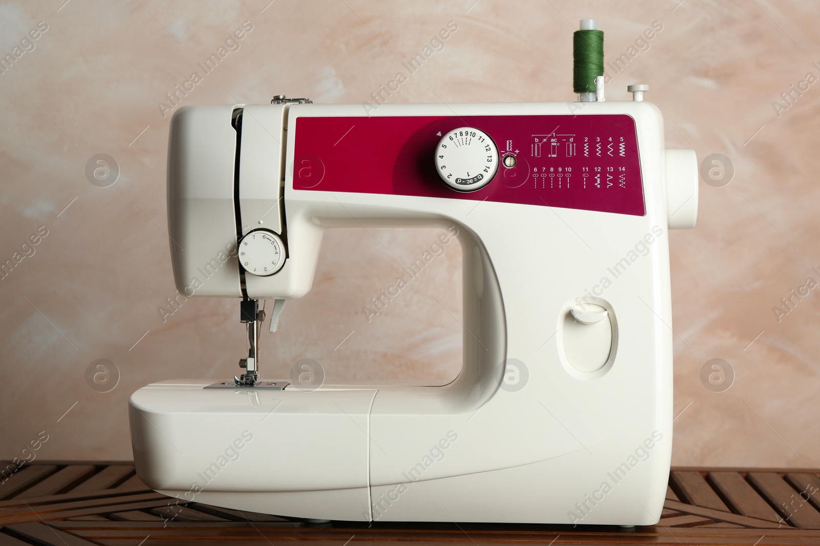 Photo of Sewing machine with spool of thread on wooden table indoors