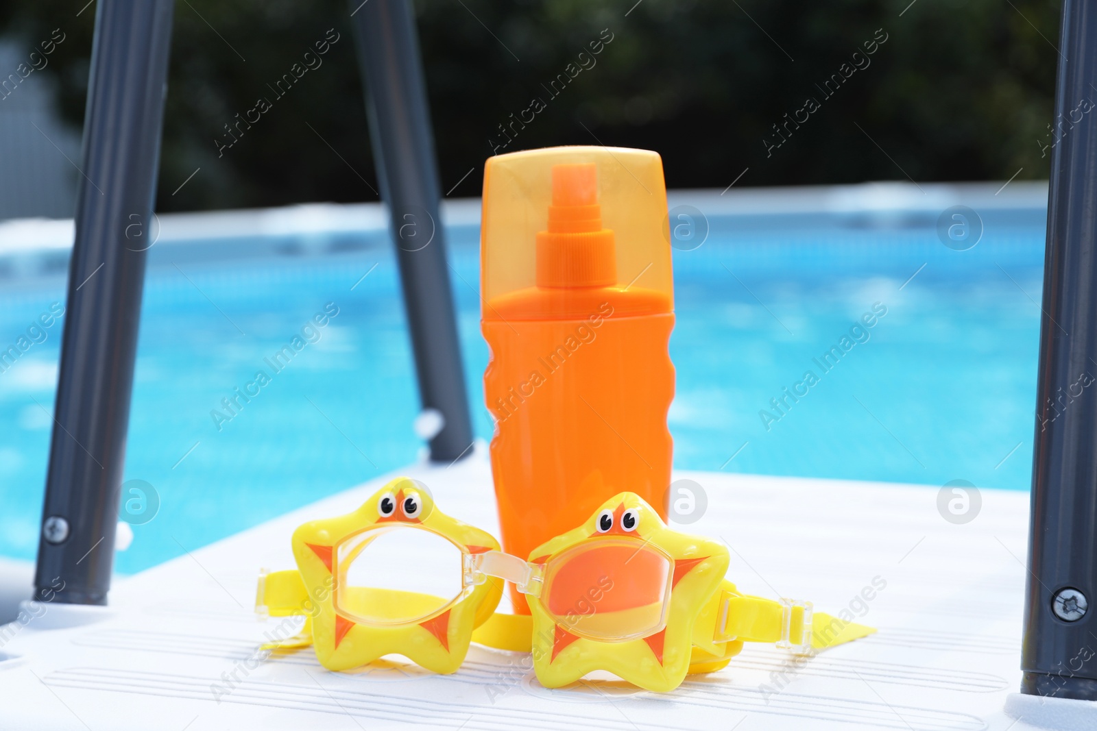 Photo of Bottle of sunscreen and swim goggles near swimming pool outdoors