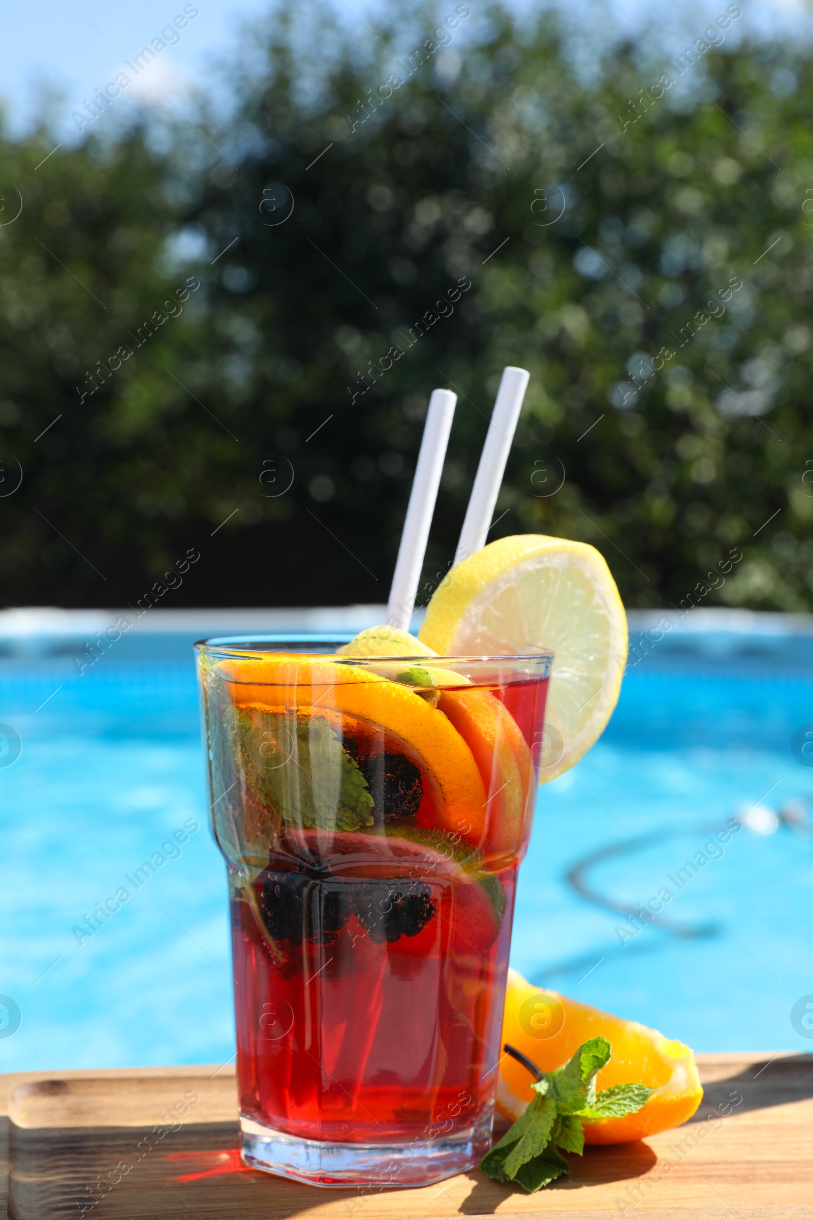 Photo of Tasty cocktail in glass near swimming pool outdoors