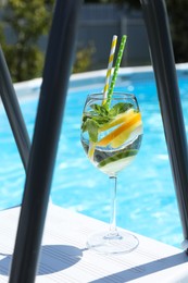 Photo of Tasty cocktail in glass near swimming pool outdoors