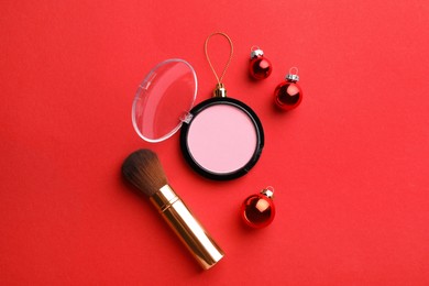 Photo of Blusher in shape of Christmas ball and brush on red background, flat lay