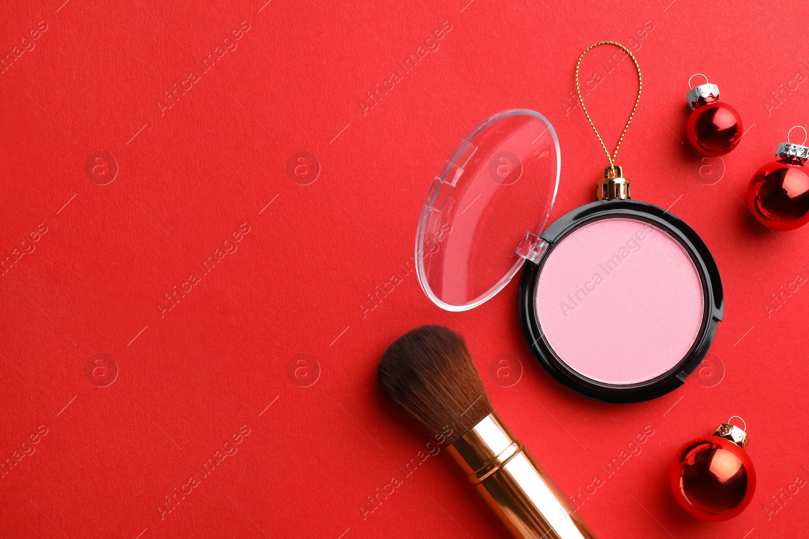 Photo of Blusher in shape of Christmas ball and brush on red background, flat lay. Space for text