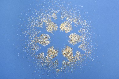 Photo of Snowflake made of golden glitter on blue background, top view