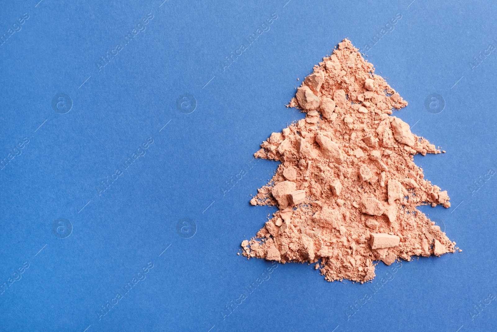 Photo of Christmas tree made with face powder on blue background, top view. Space for text