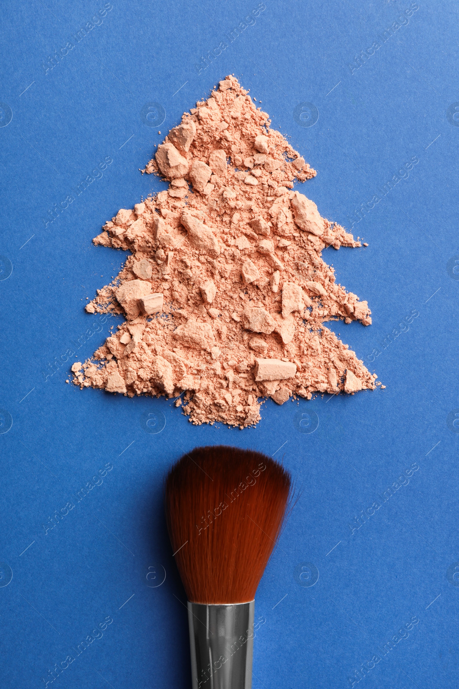 Photo of Christmas tree made with face powder and brush on blue background, top view