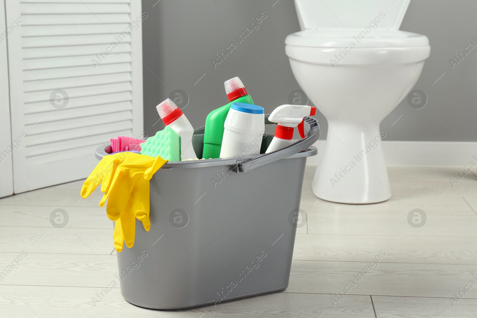 Photo of Bucket with different toilet cleaners, rag, sponge and gloves in bathroom