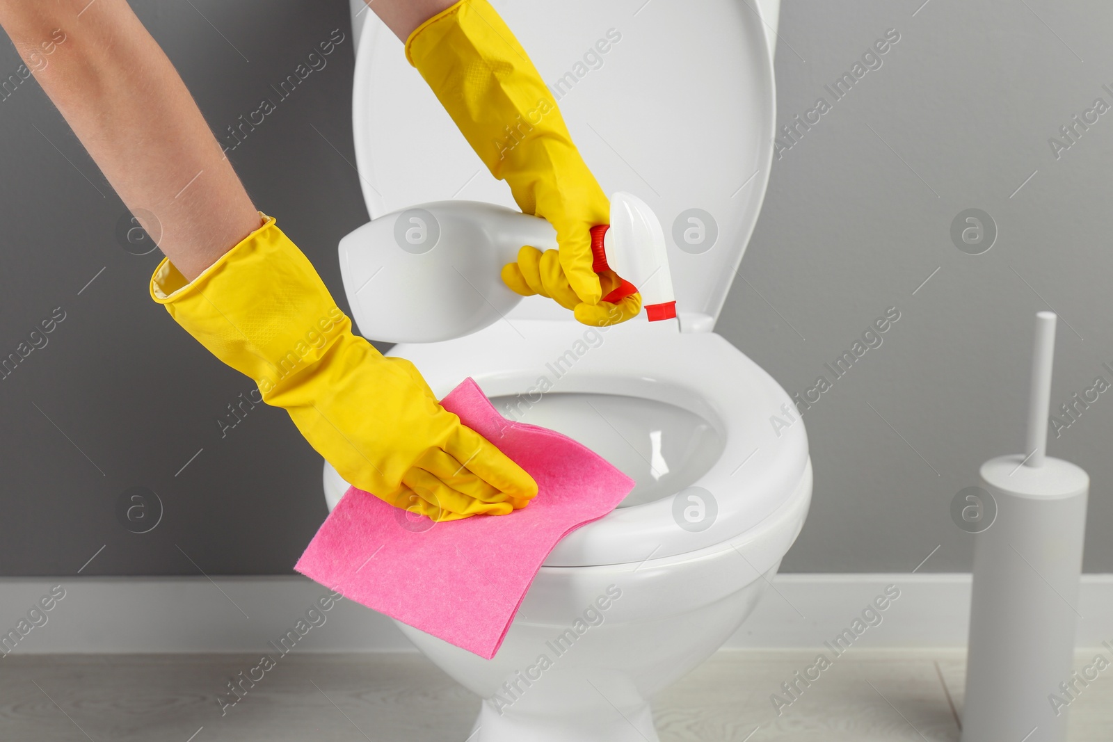 Photo of Woman with spray and rag cleaning toilet seat in bathroom, closeup