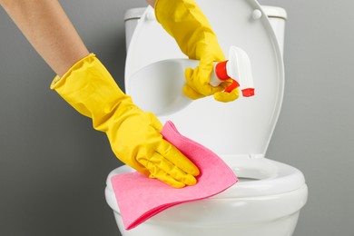 Photo of Woman with spray and rag cleaning toilet seat in bathroom, closeup