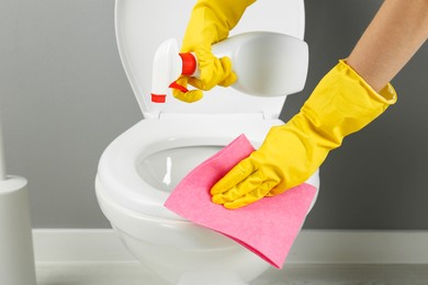 Photo of Woman with spray and rag cleaning toilet seat in bathroom, closeup