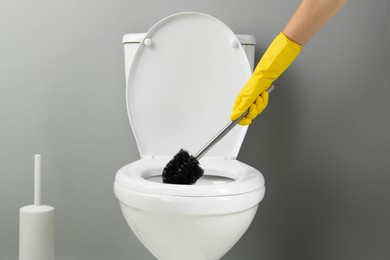 Photo of Woman cleaning toilet with brush in bathroom, closeup